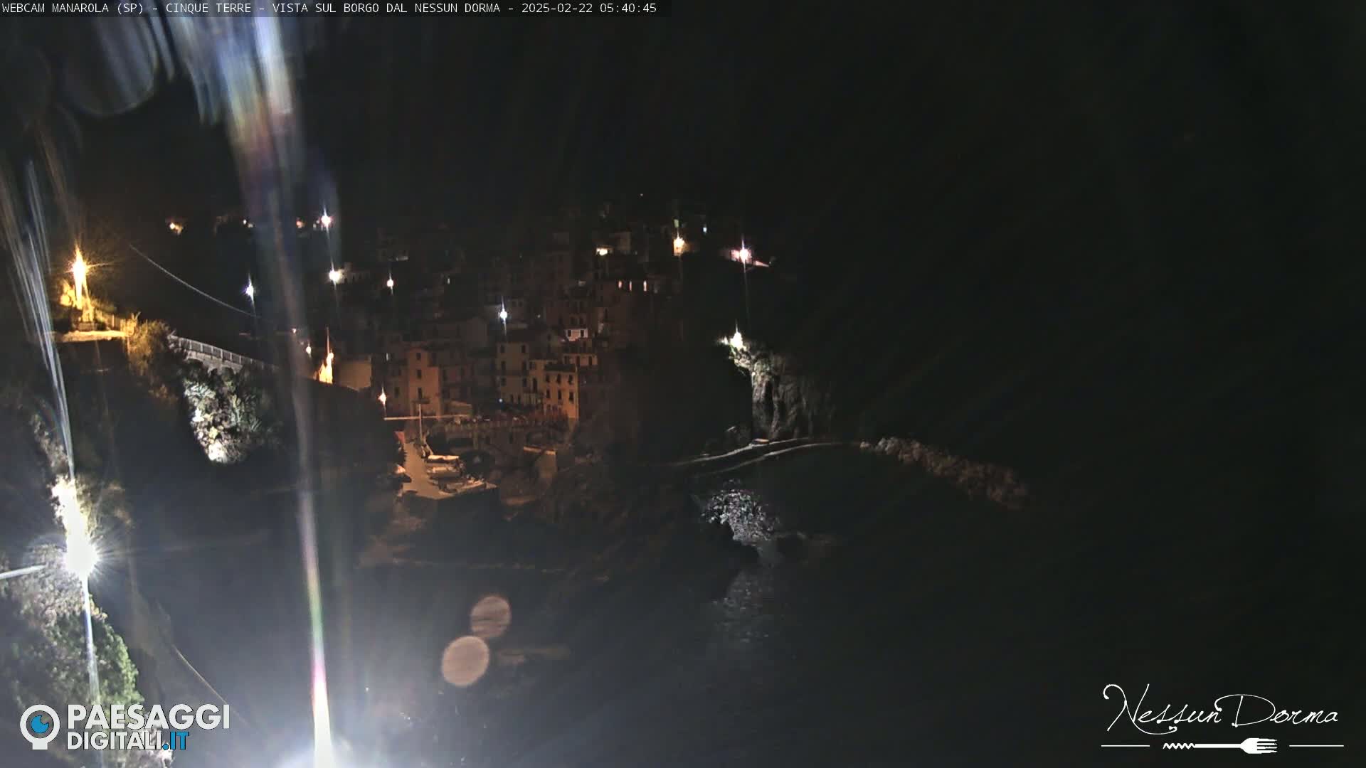 A nighttime view of a coastal town nestled on a cliffside, illuminated by scattered lights.