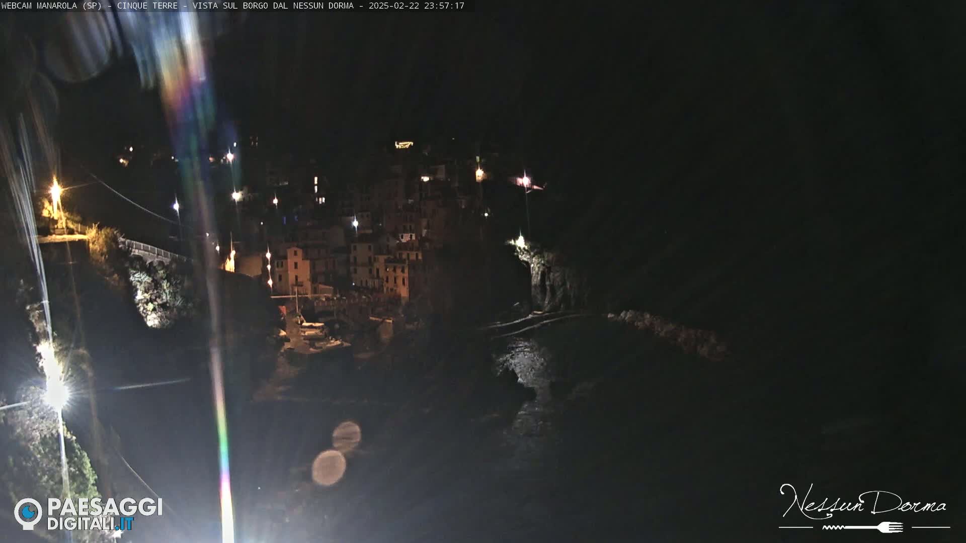 A nighttime, coastal village with buildings lit up along a dark, rocky shoreline.