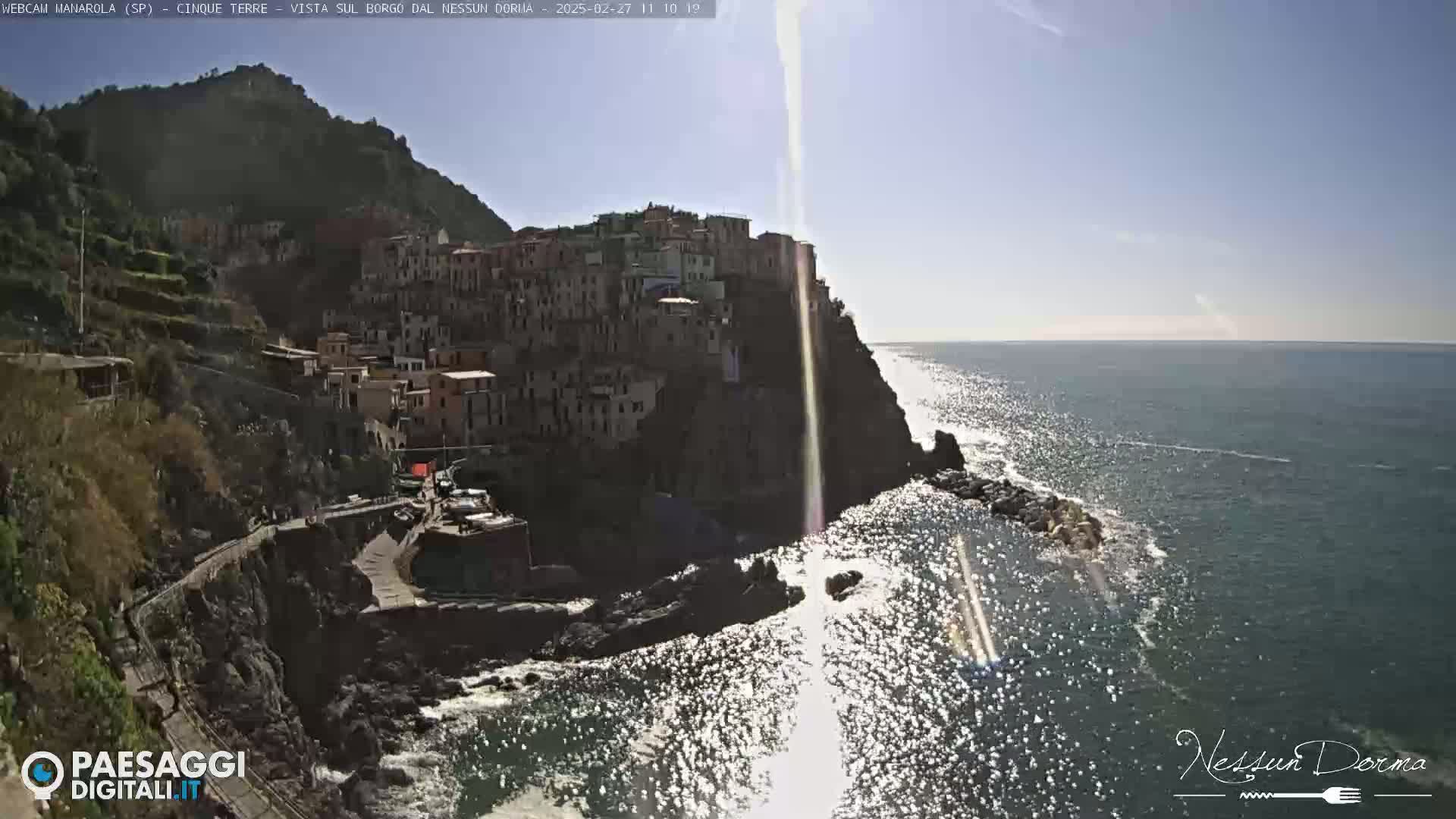 A sun-drenched coastal village clings to a steep cliffside overlooking a sparkling sea.