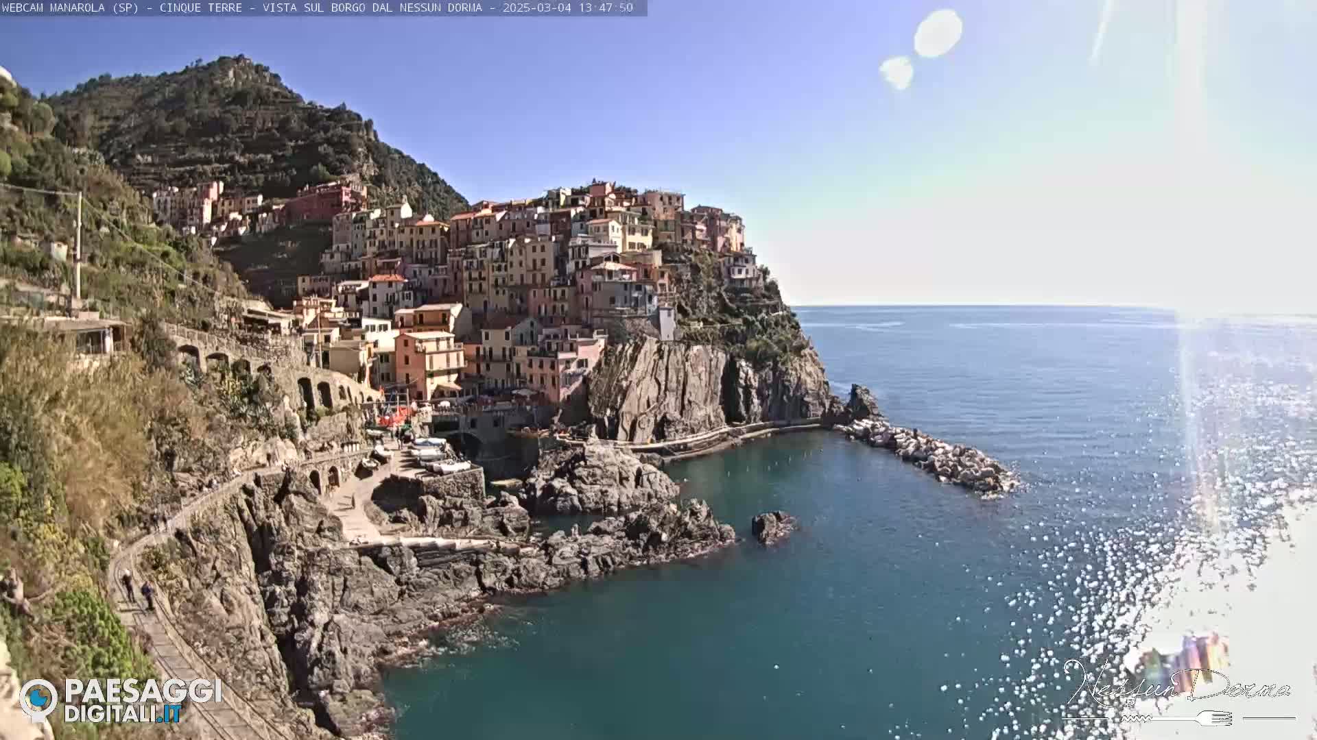 A picturesque coastal town, built on a cliffside overlooking a calm, clear sea, under a bright sunny sky.