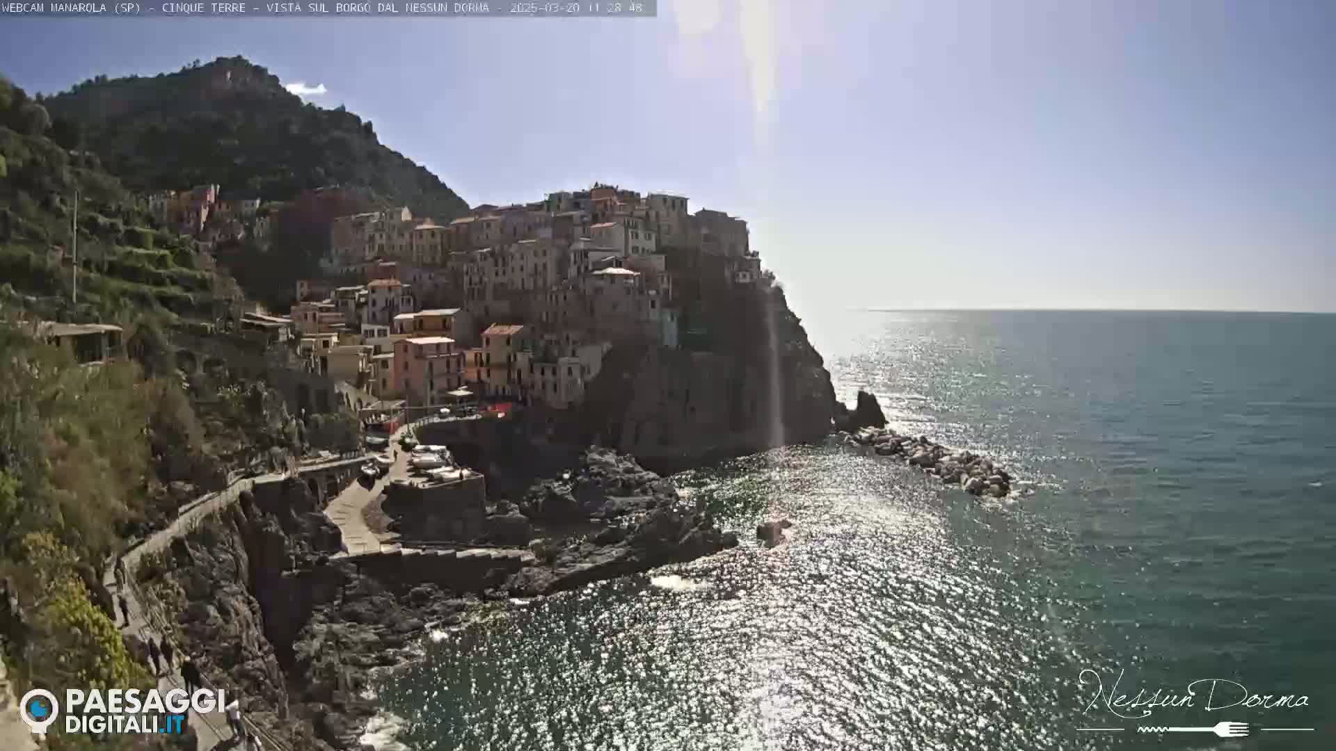 A sunlit coastal village clings to a steep hillside overlooking a sparkling sea.