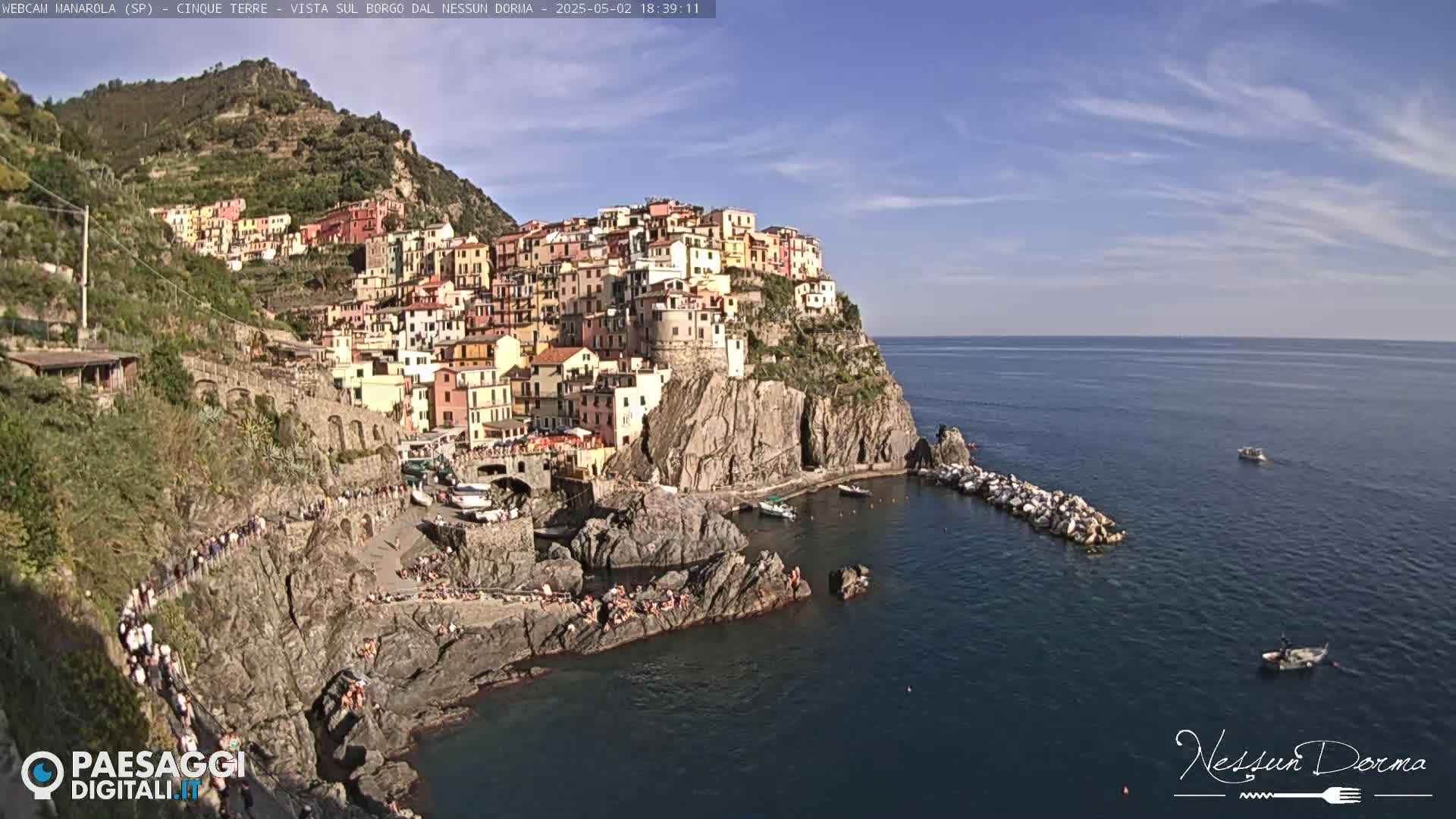 A picturesque coastal town with colorful buildings clinging to a cliffside overlooking a calm sea under a mostly sunny sky.
