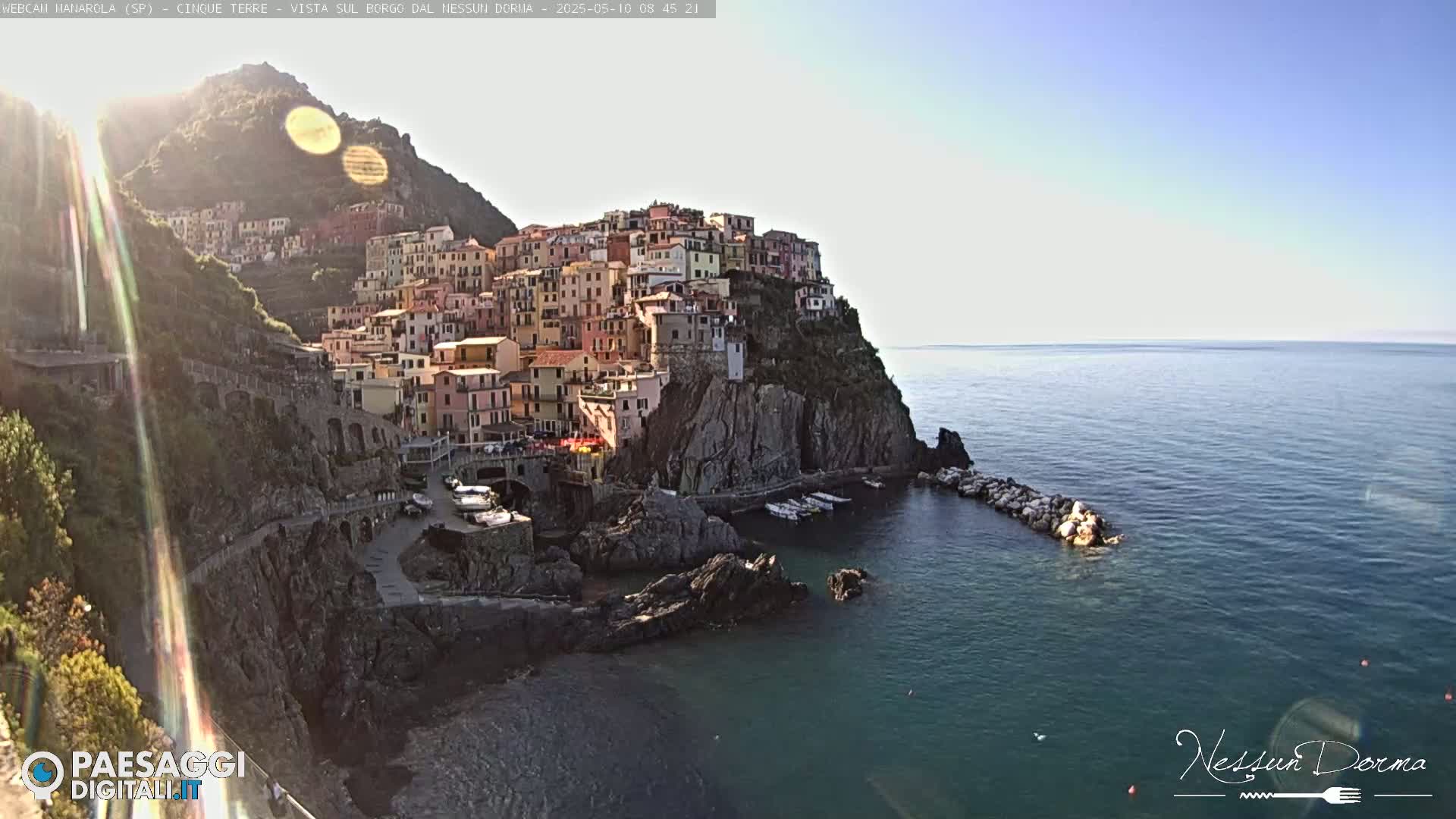 A sun-drenched coastal town clings to a cliffside overlooking a calm sea.