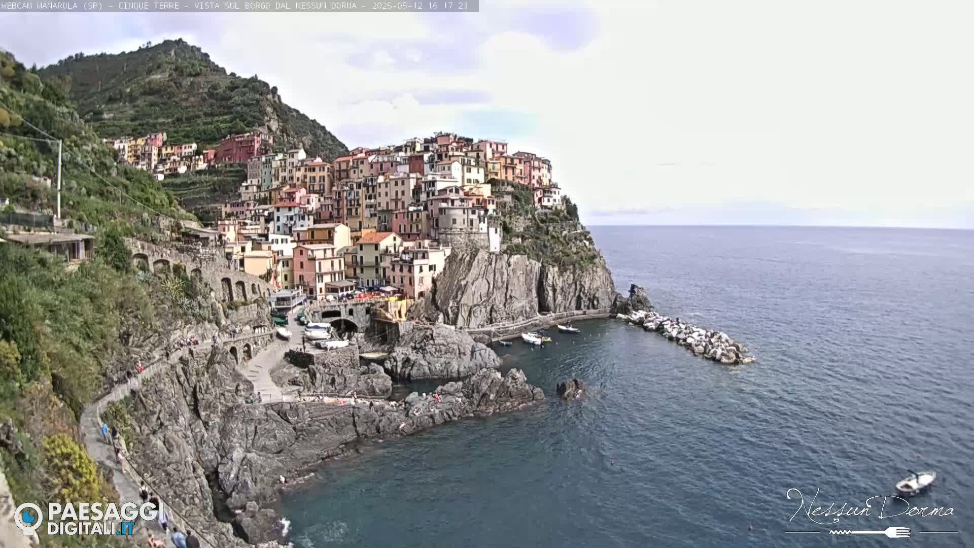 A picturesque coastal town with colorful buildings clinging to a cliffside overlooking a calm sea under a partly cloudy sky.