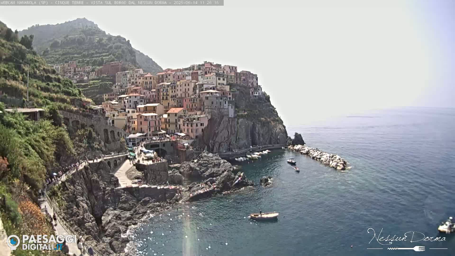 A picturesque coastal town clinging to a cliffside overlooks a calm sea, under a bright, clear sky.