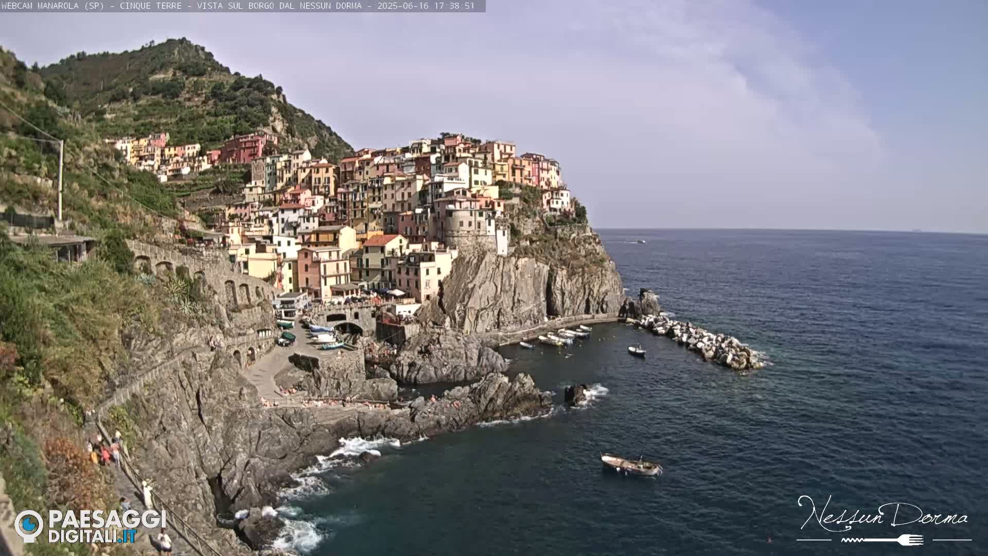 A picturesque coastal town clinging to a rocky cliffside, with a calm sea and sunny skies.