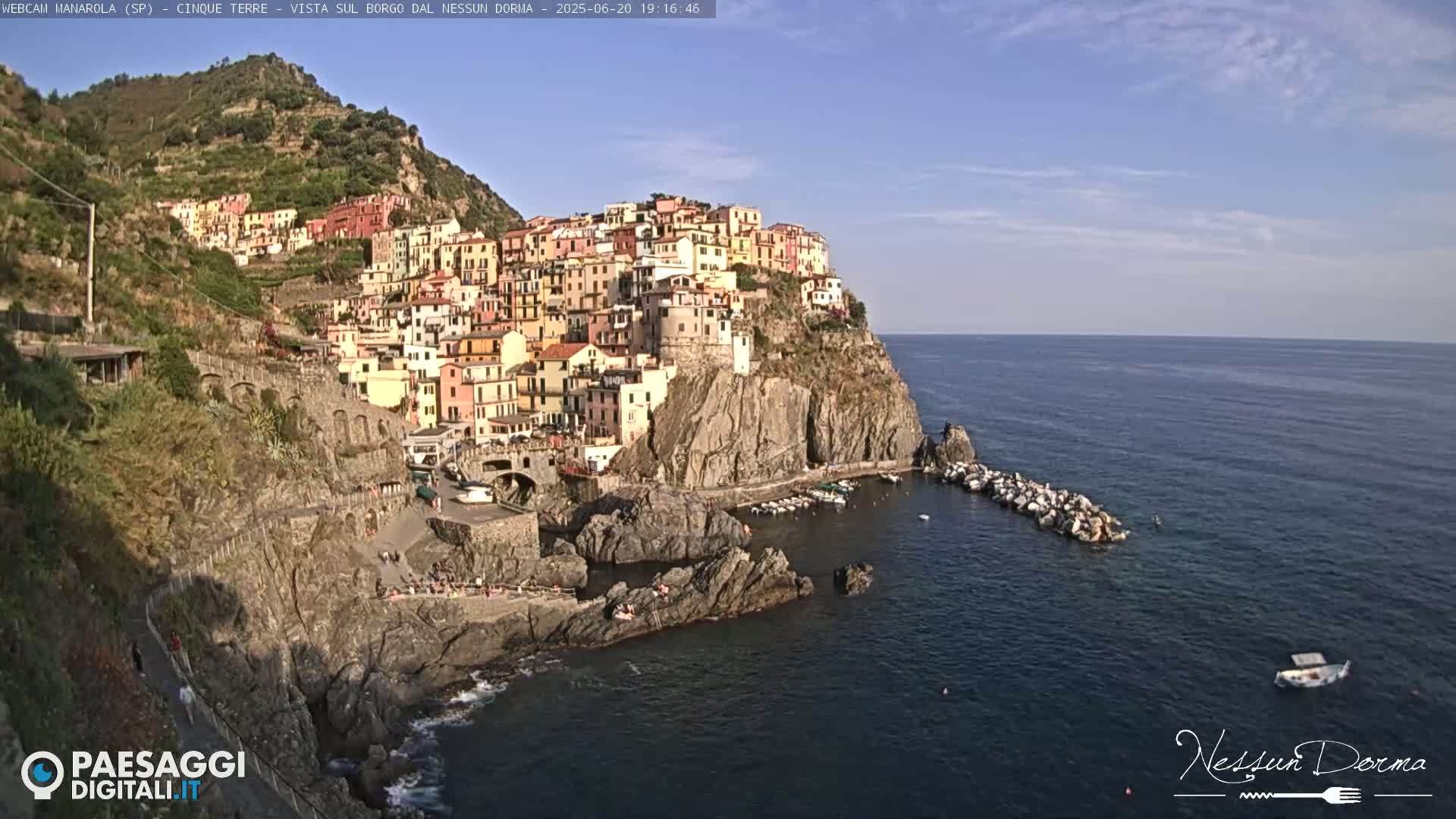 A colorful village clings to a steep cliffside overlooking a calm blue sea under a clear sky.