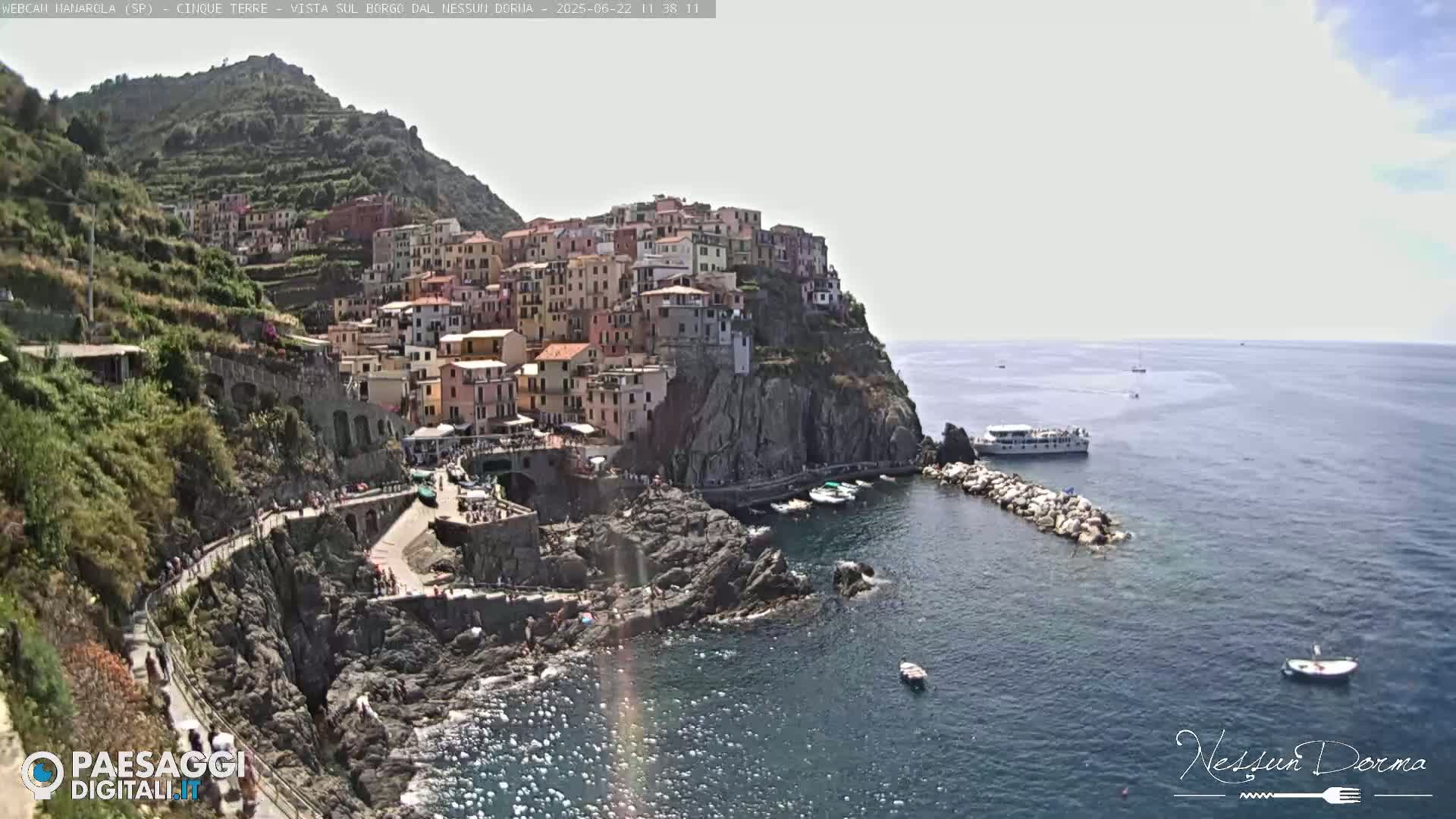A picturesque coastal town clings to a cliffside overlooking a calm sea on a bright, sunny day.