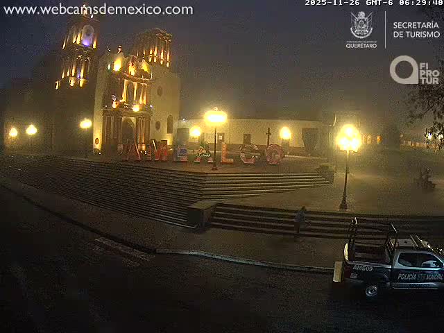 An ornate, brightly lit historic building with two prominent towers stands behind a wide set of steps, fronted by large colorful letters spelling "AMELO" and illuminated by multiple streetlights on a clear night.