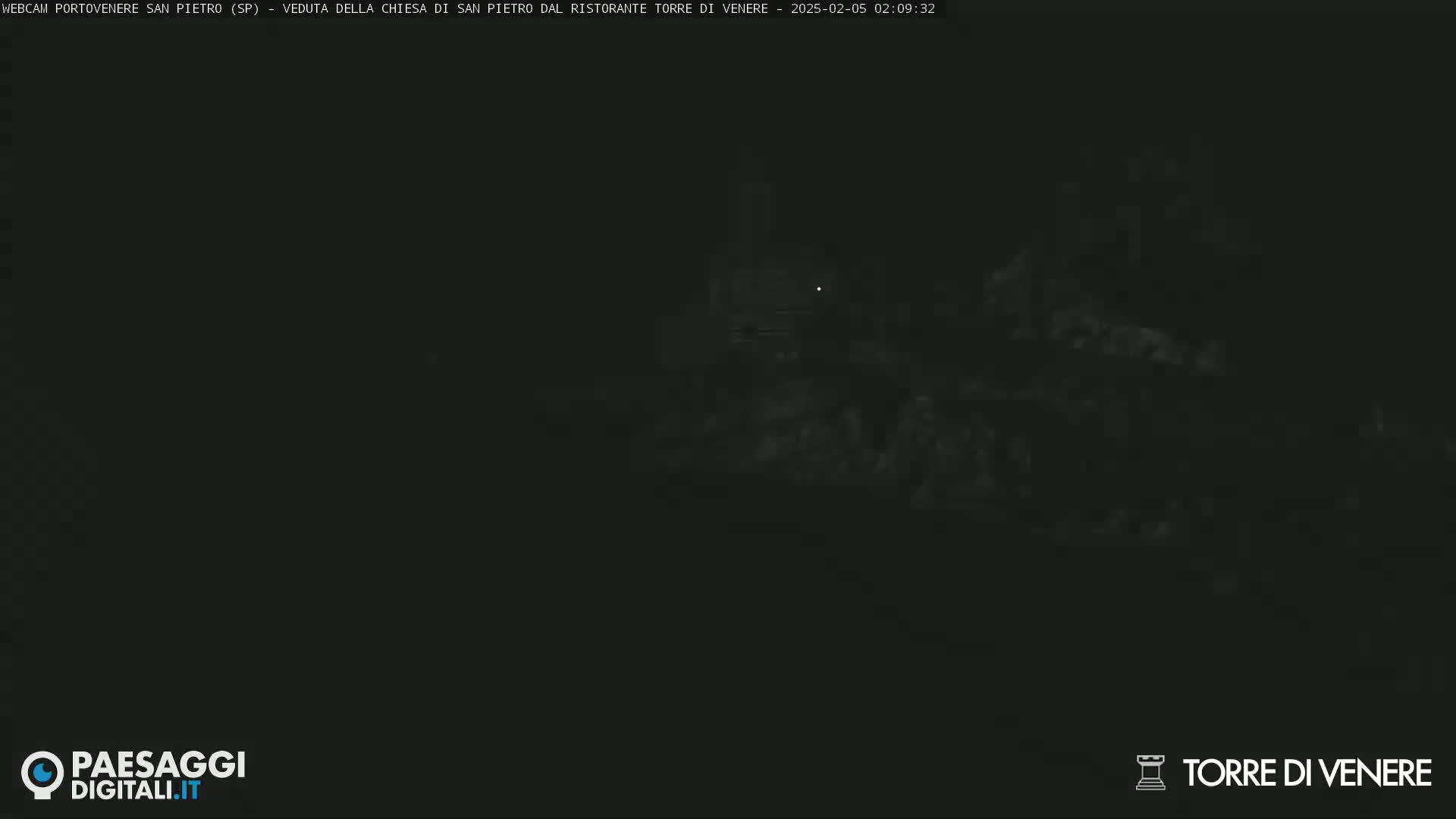 A dark, nighttime scene shows indistinct shapes of buildings and land, possibly under a clear sky.