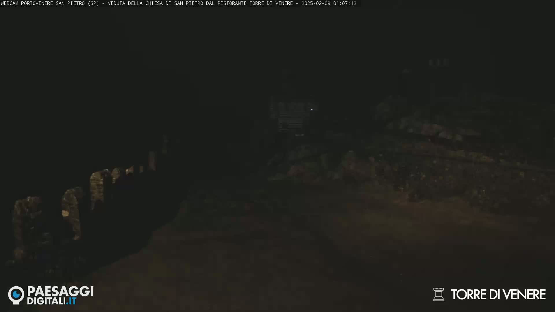 A dark, nighttime scene shows indistinct shapes and a dimly lit area, possibly outdoors.