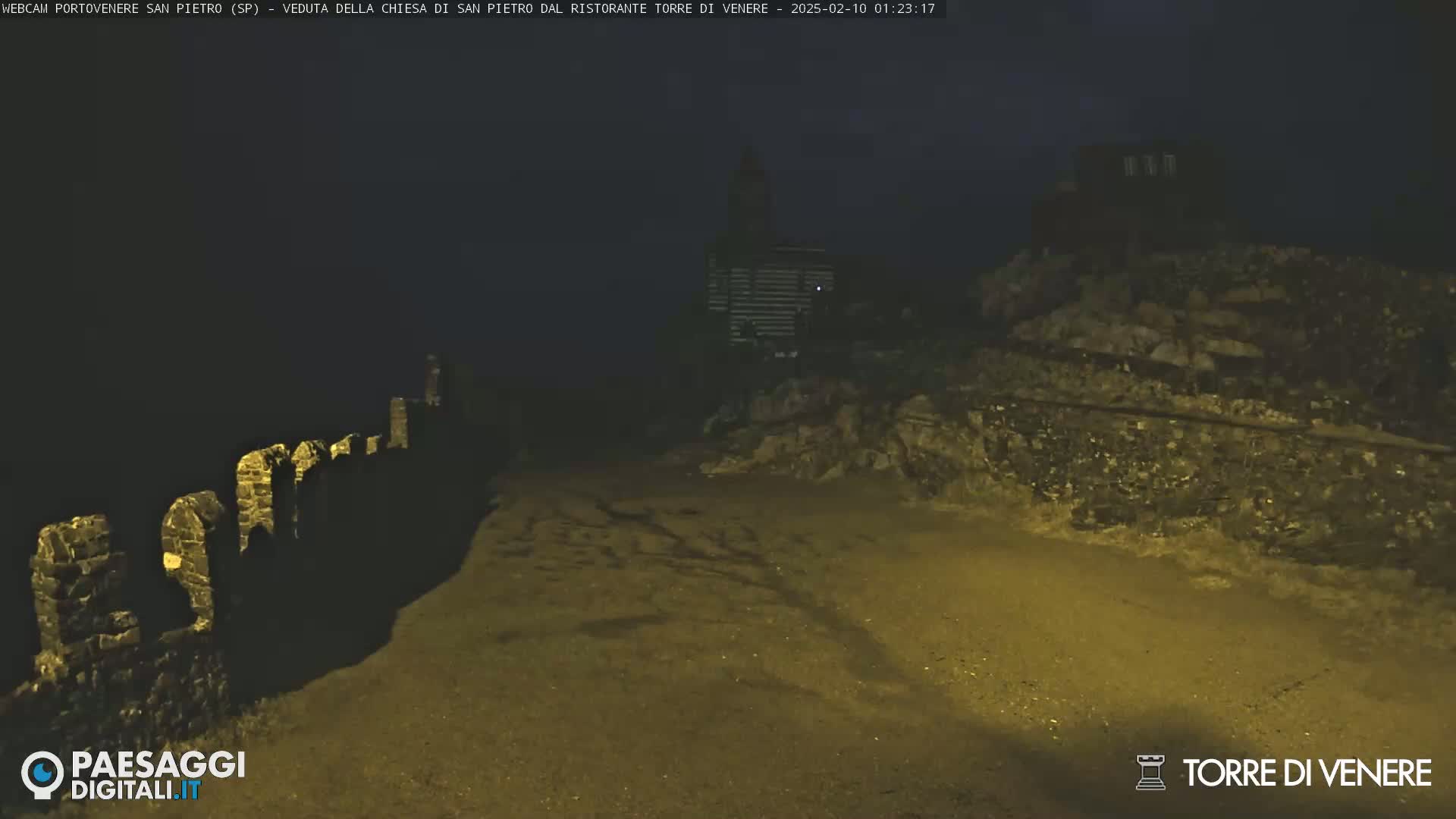 A nighttime view shows a stone wall and a building in the distance under dark, possibly overcast conditions.