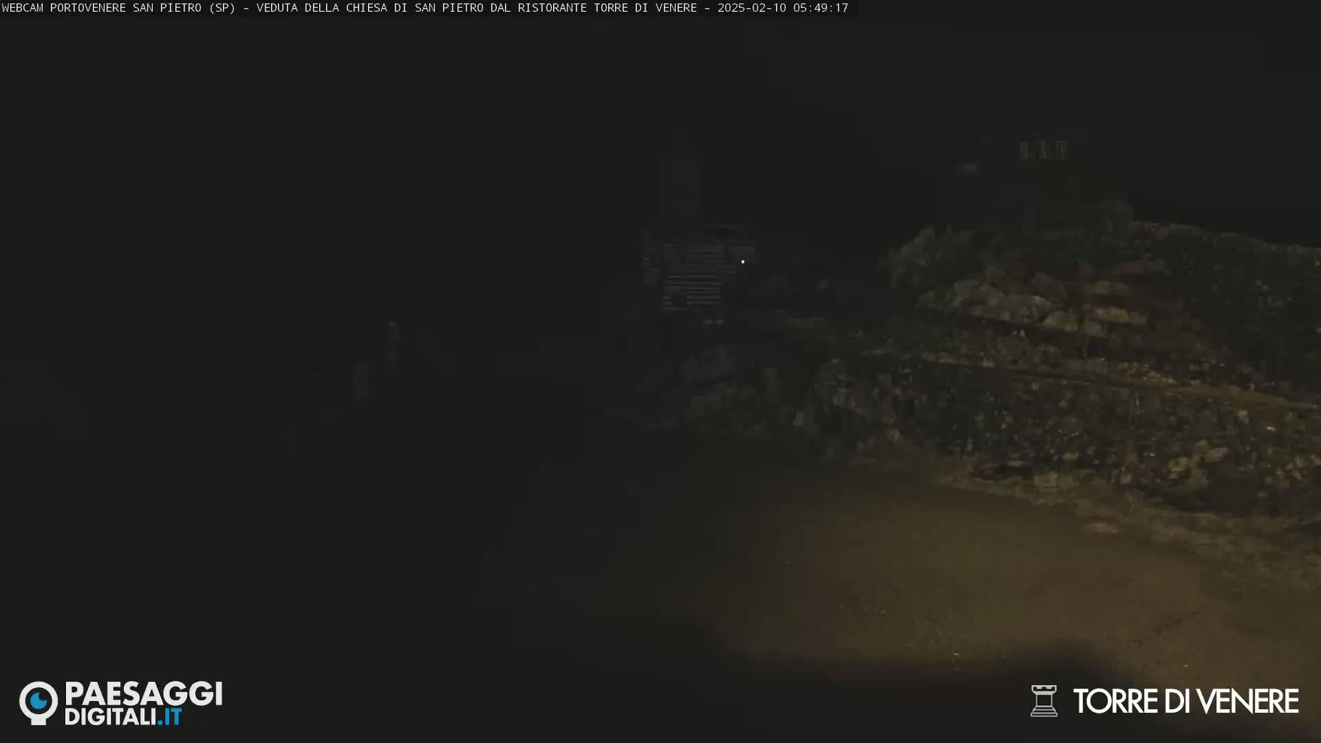 A dark, nighttime scene shows a dimly lit stone structure and a road.
