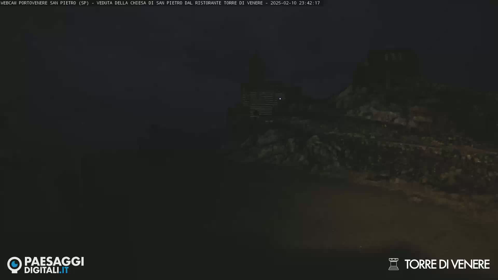 A dark, nighttime view of a stone structure, possibly a building or ruins, on a rocky hillside.