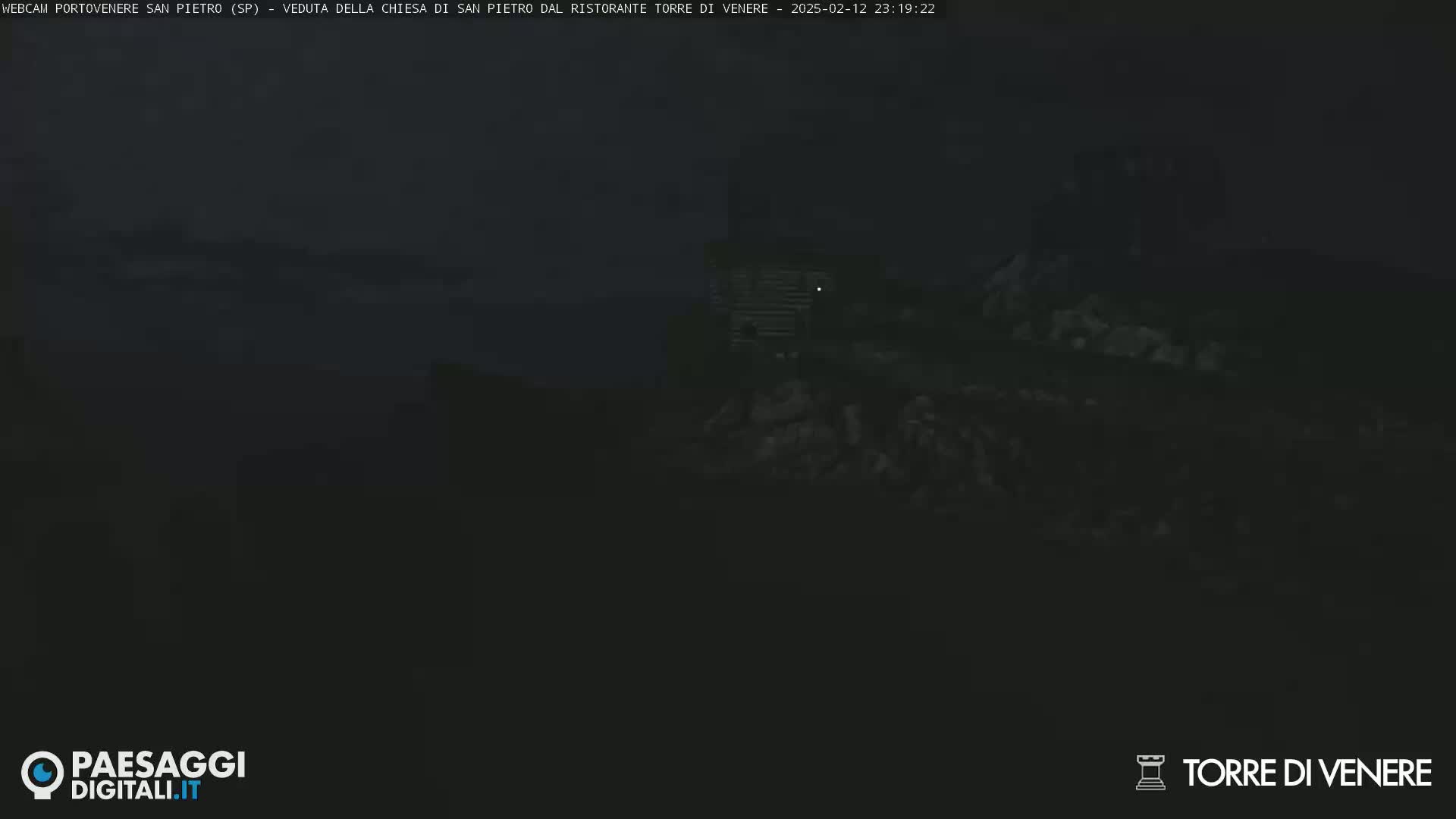 A dark, nighttime scene shows a dimly lit structure atop a rocky hill under a cloudy sky.