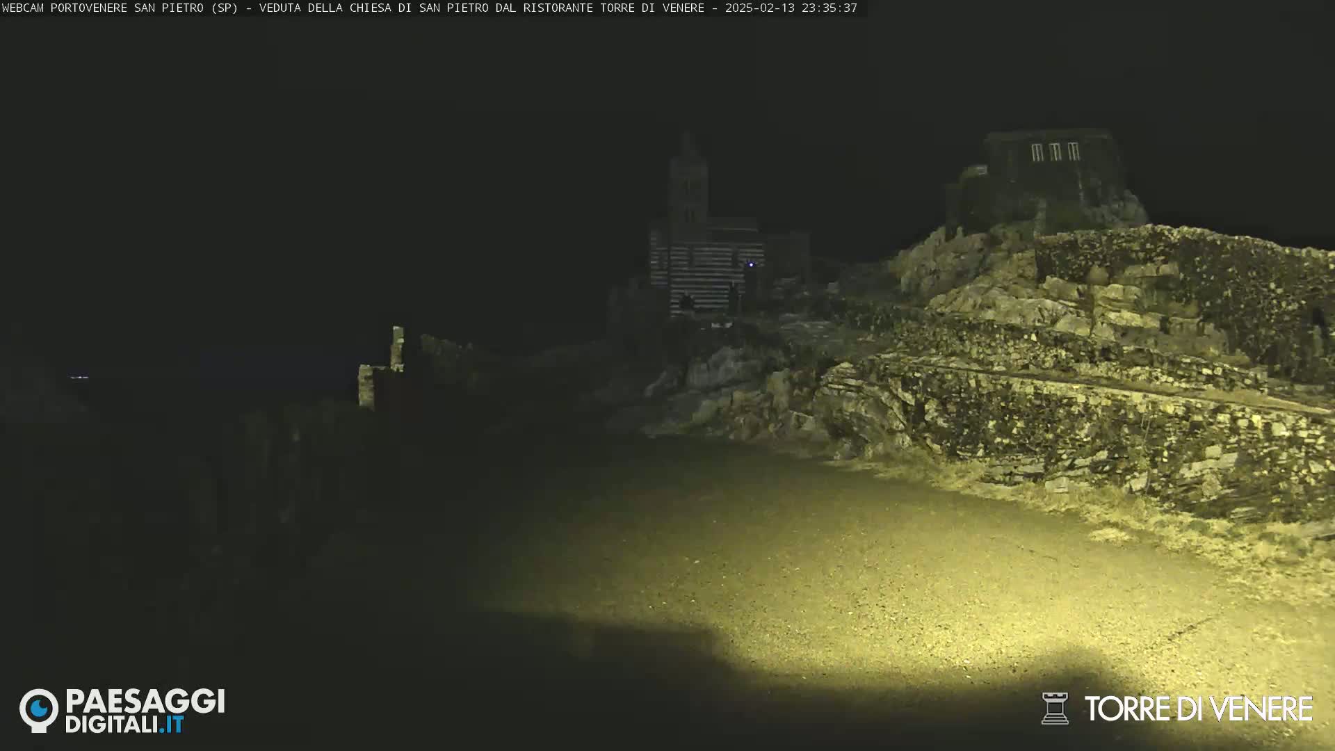 A nighttime, low-light view of a rocky, hilly landscape with buildings and a church visible in the distance.