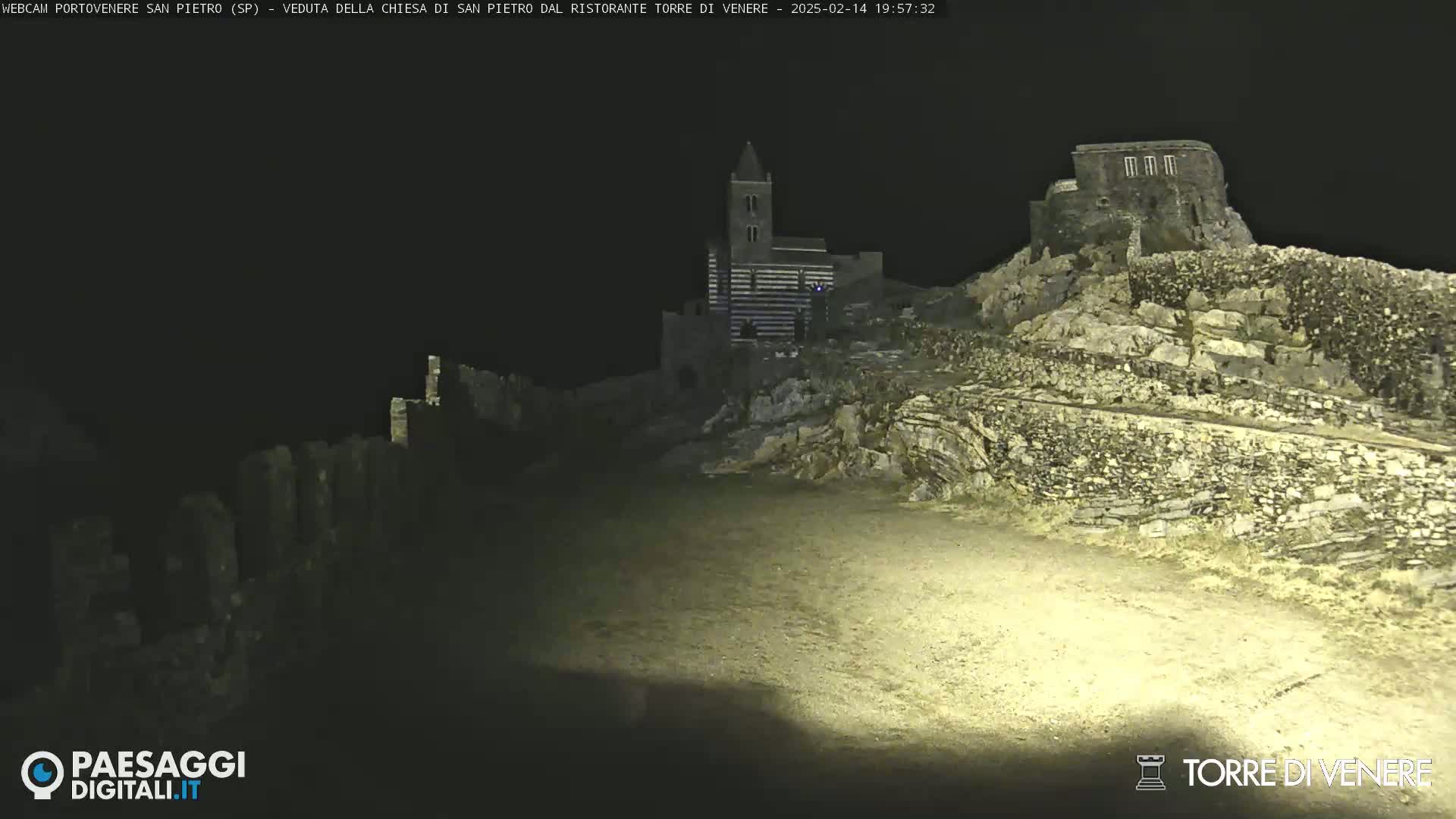 A nighttime, low-light view of stone structures, including a church and ruins, atop a hill.