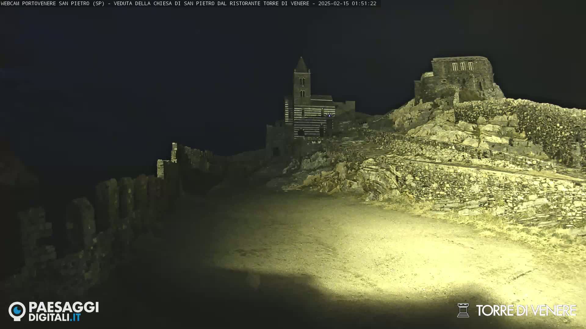 A nighttime view of stone structures, including a striped church, situated on a rocky hillside under a dark sky.