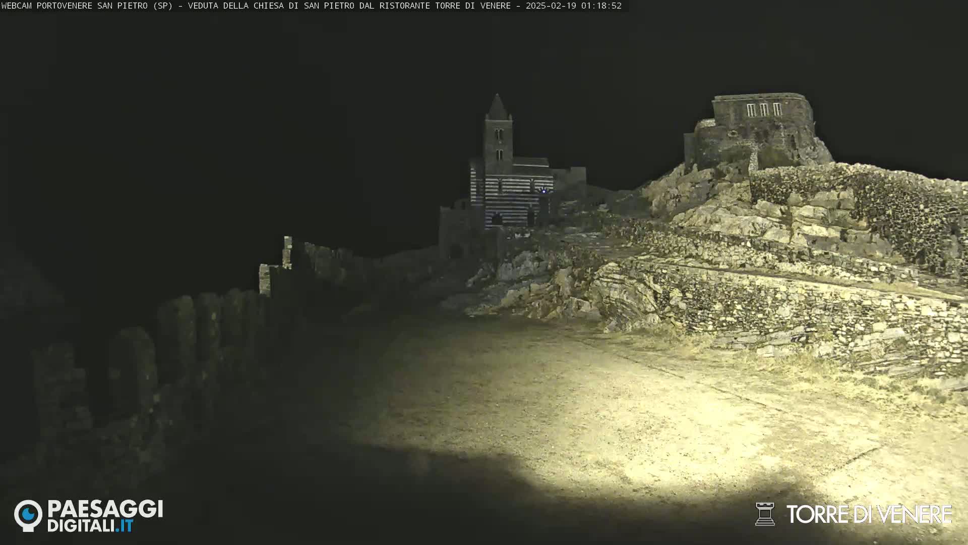 A nighttime, low-light view of stone structures, including a church-like building on a hilltop.