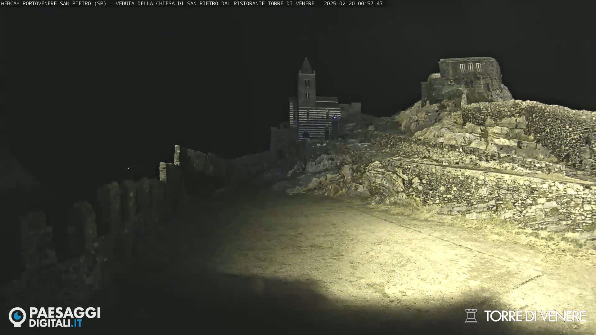 A nighttime view of stone structures, including a church and ruins, illuminated by artificial light.