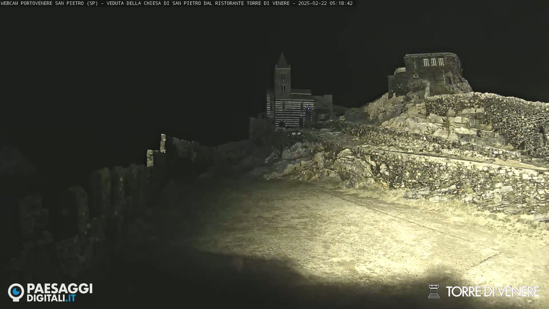 A nighttime, low-light view of stone structures, including a church, situated on a rocky hilltop.