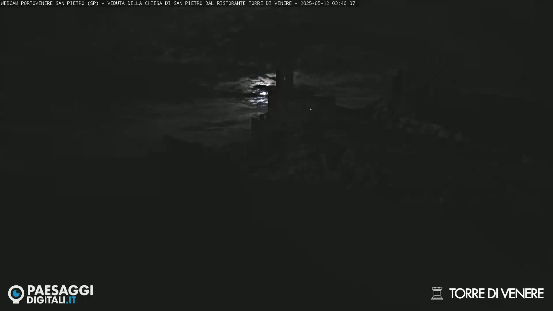 A dark, nighttime scene shows a dimly lit structure under a cloudy sky illuminated by a bright moon.