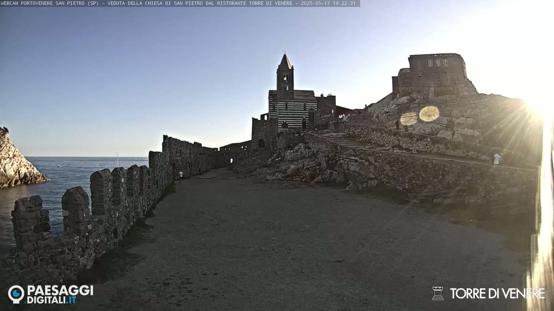 A rocky coastal area with a striped church and stone walls, bathed in the late afternoon sun.