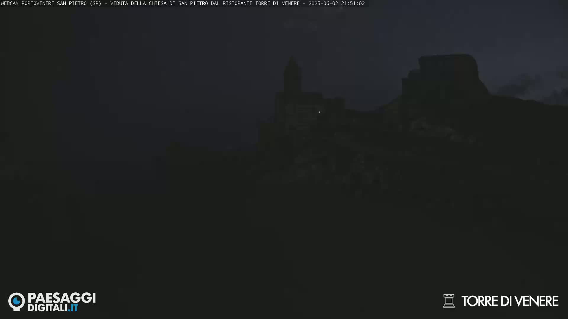 A dark, nighttime image shows a dimly lit stone structure, possibly a church or castle, silhouetted against a dusky sky.
