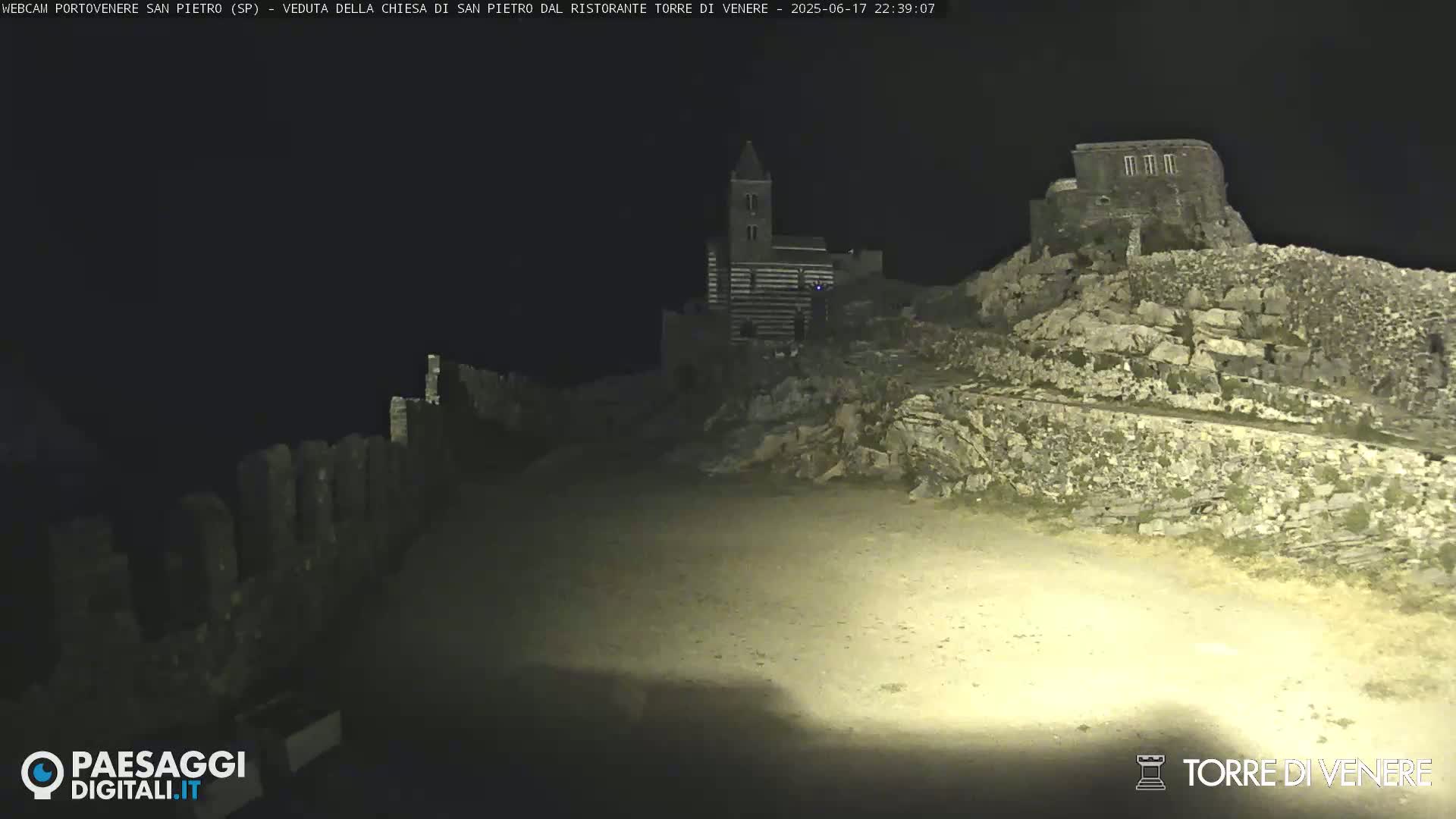 A nighttime, low-light view of a stone church and ruins on a hilltop.