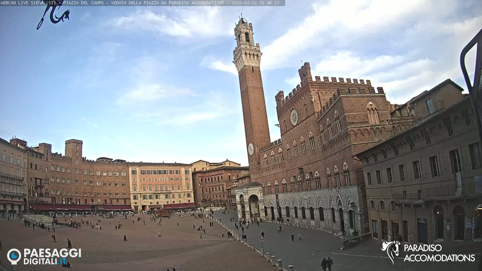 A large brick plaza is shown with several buildings surrounding it, under a partly cloudy sky.