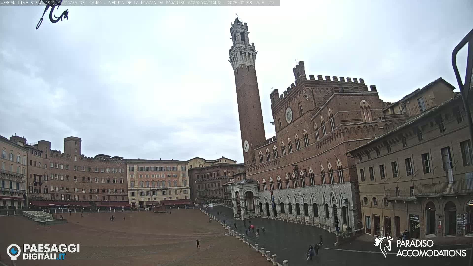 A large, brick public square in Italy, possibly Siena, is shown on an overcast day, with a tall, slender tower and a large brick building prominently featured.