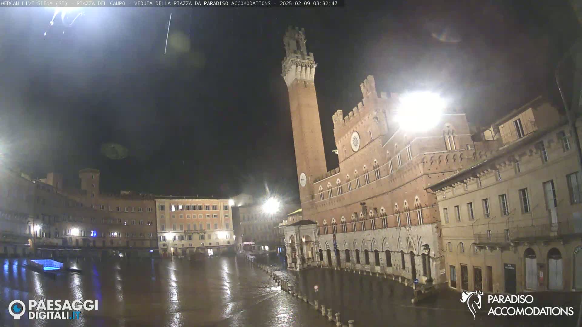 A flooded plaza at night is surrounded by historic brick buildings under a dark, overcast sky.