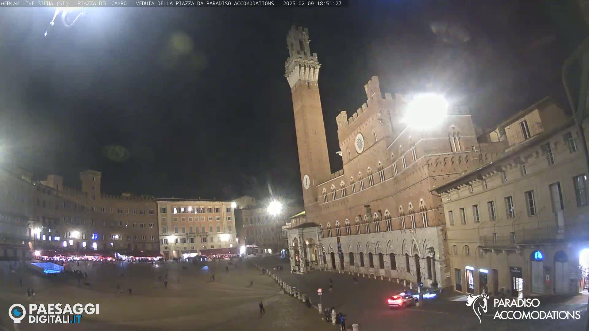 A nighttime view of a large, mostly empty town square in Italy, surrounded by historical buildings under a clear, dark sky.