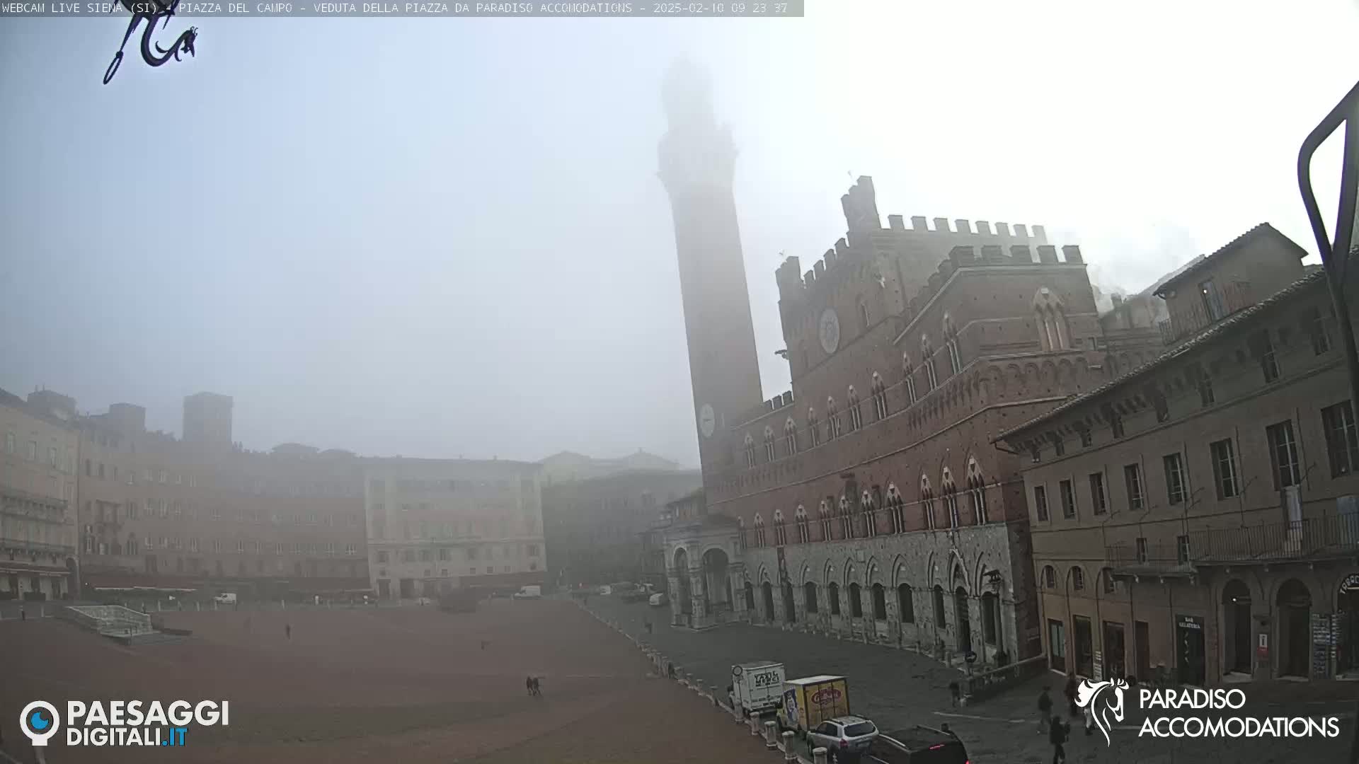 A foggy view of a large, brick piazza in Italy, dominated by a tall tower and a grand palace-like building.