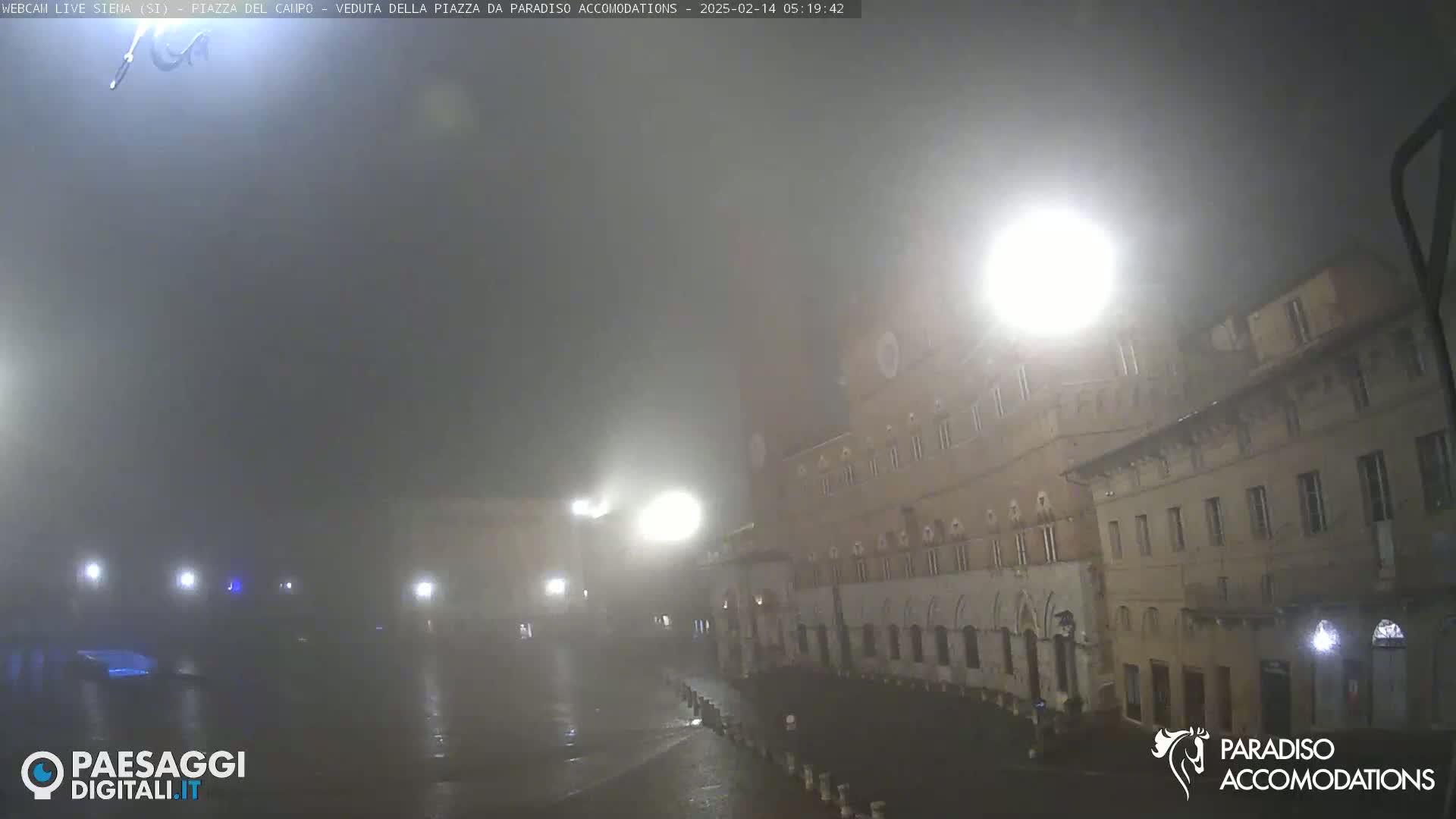 A foggy, nighttime view of a town square with several buildings, some with lights visible.