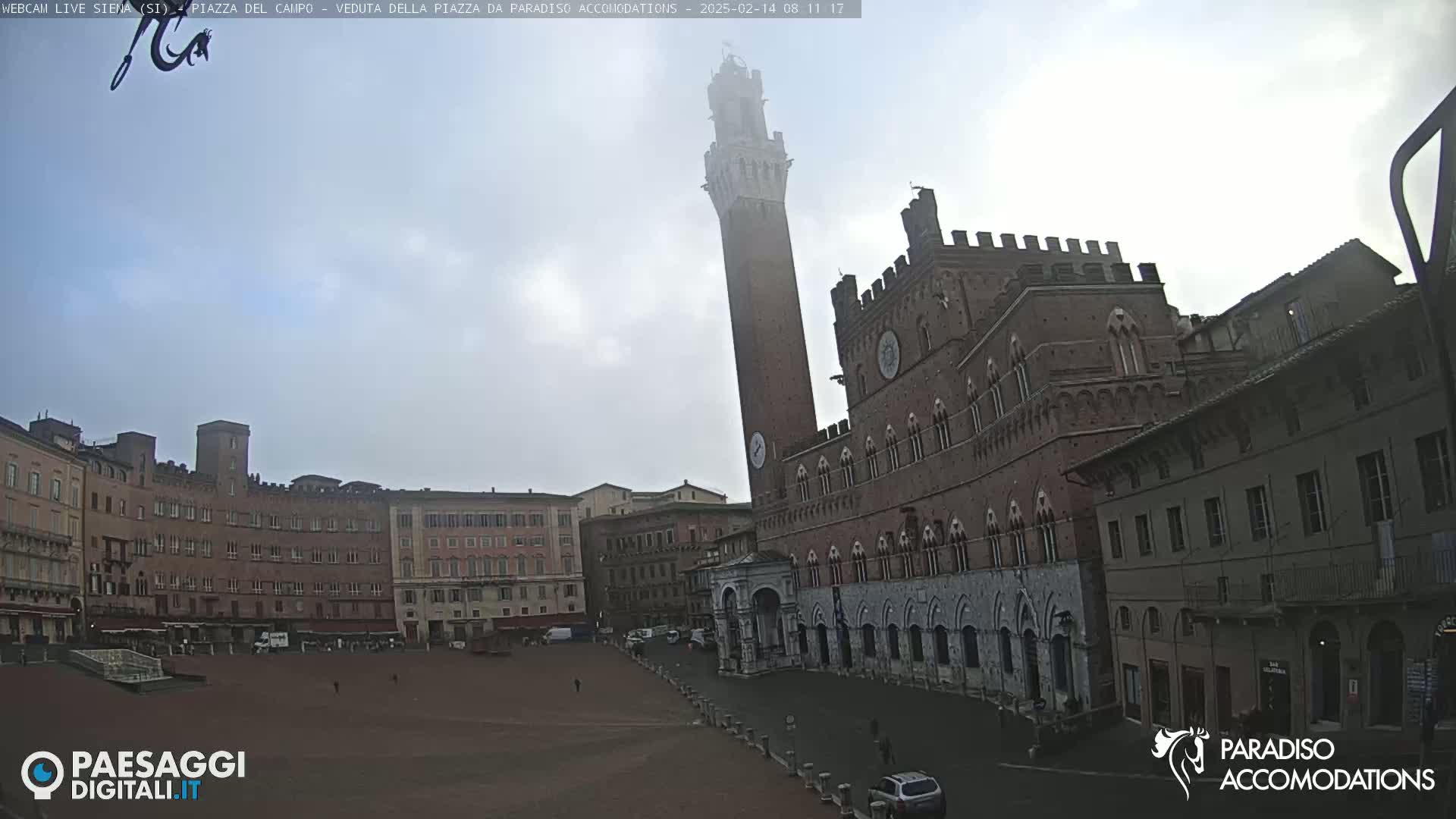 A large, empty square in front of a tall brick tower and a brick palace under a cloudy sky.