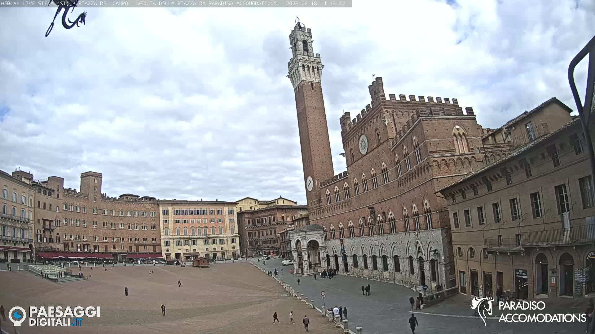 A large, mostly empty brick plaza is surrounded by medieval-style buildings under a partly cloudy sky.