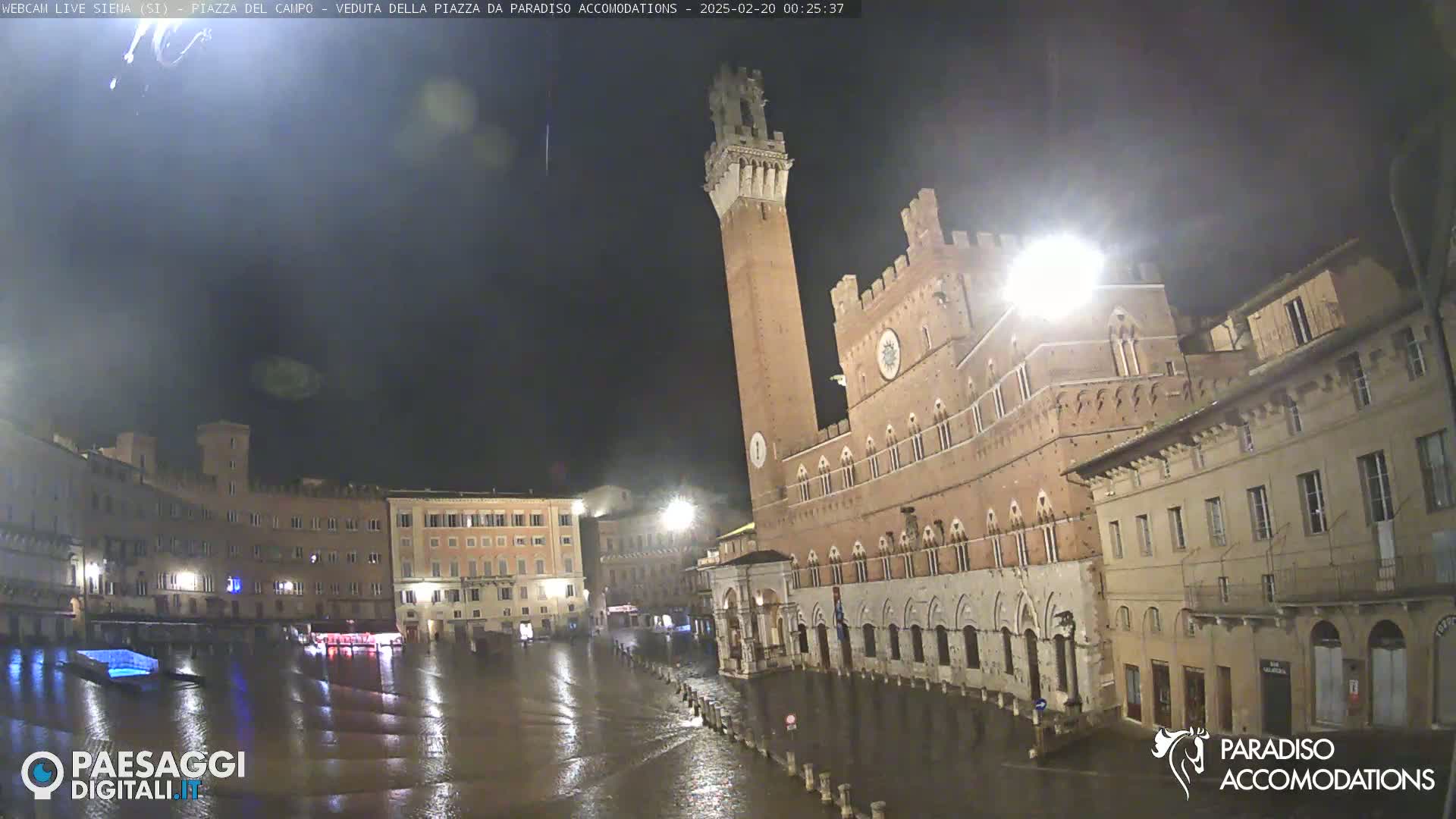 A large, brick piazza in Italy is flooded under a dark, nighttime sky.