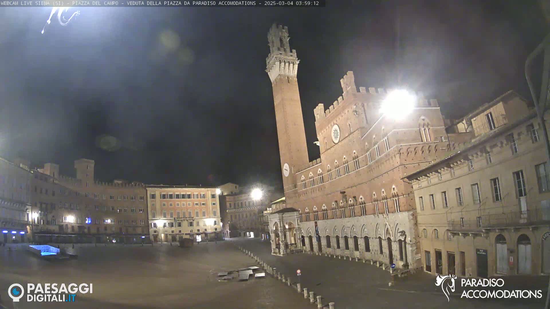 A nighttime view of a large, empty town square surrounded by historic buildings, including a tall brick tower.