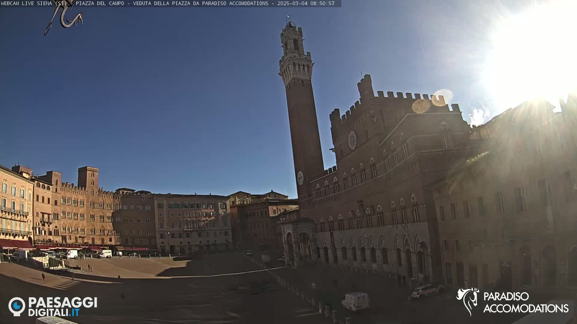 A sunny day reveals a large, brick piazza in Italy, surrounded by historical buildings, including a tall tower.