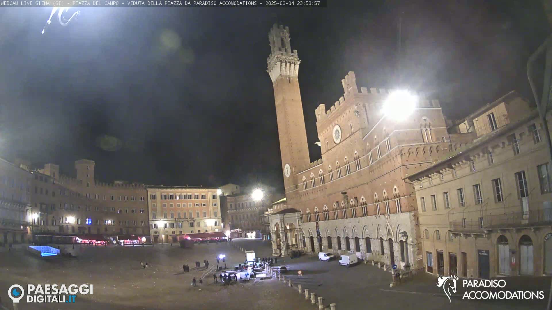 A nighttime view of a large, mostly empty plaza with historical buildings, including a tall tower and a grand palace, under a dark, clear sky.