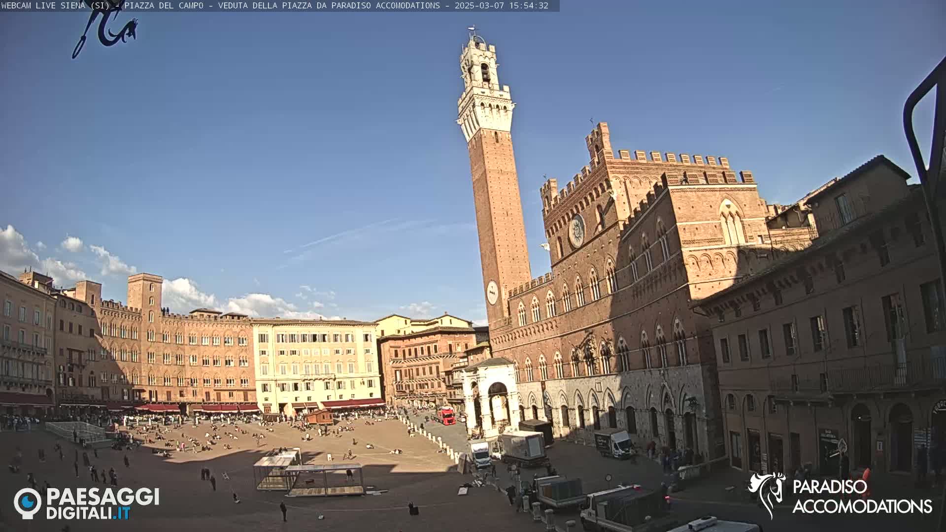 A sunny day reveals a large, mostly empty plaza surrounded by medieval-style buildings, including a tall brick tower and a large palace.