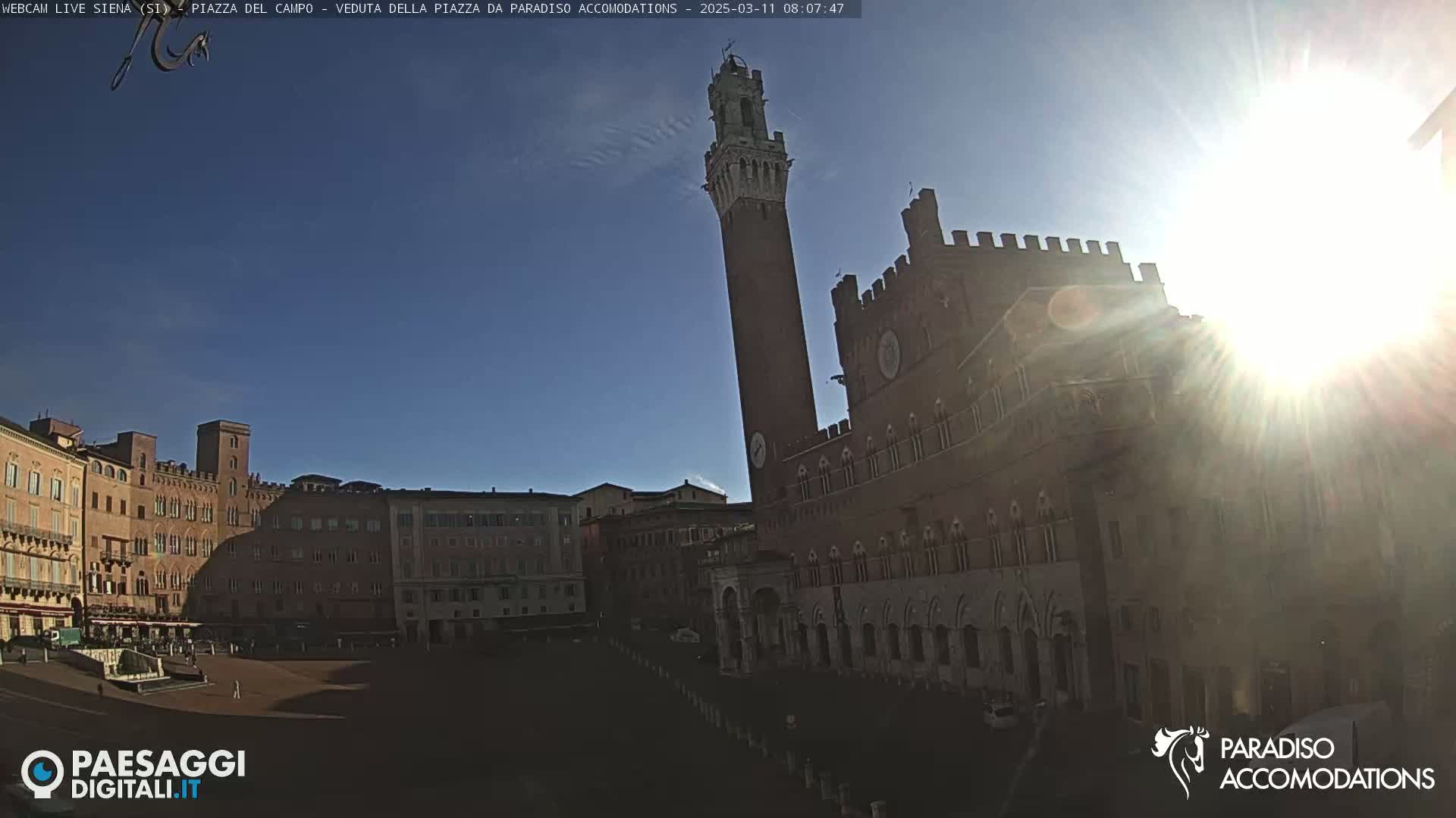 A sunny day reveals a large, brick plaza with a tall tower and a grand palace in the background, surrounded by historic buildings.