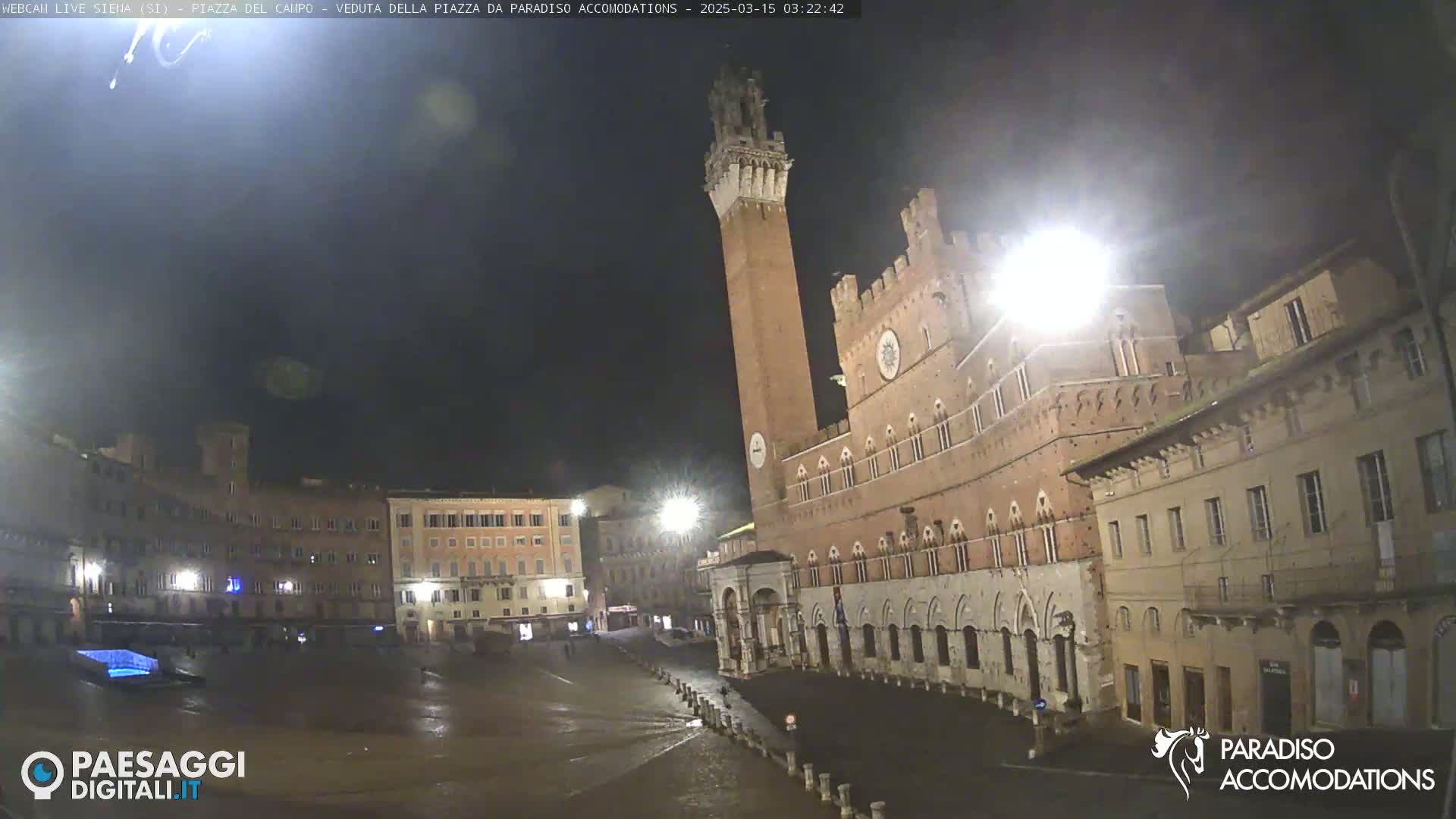 A nighttime view of a large, empty plaza with historic brick buildings surrounding it, under a dark sky.