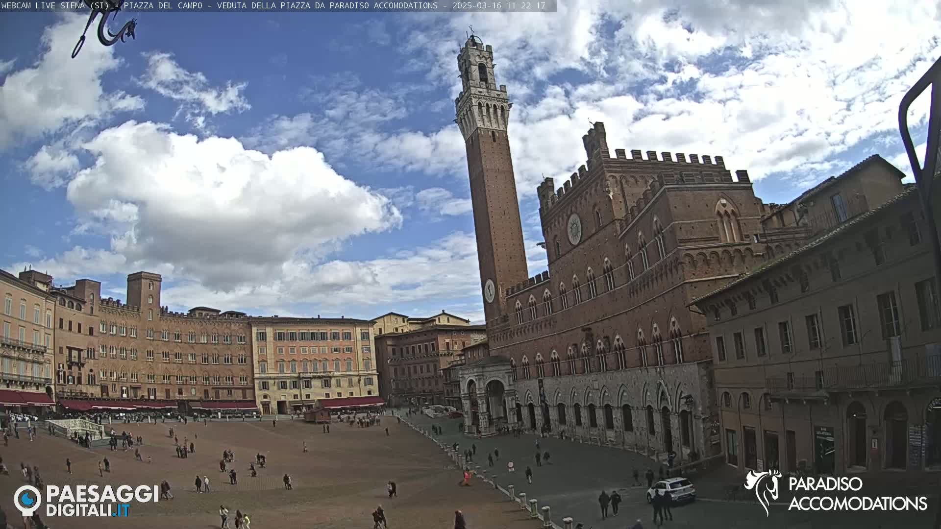 A large, open square in a city is surrounded by historic brick buildings, under a partly cloudy sky.