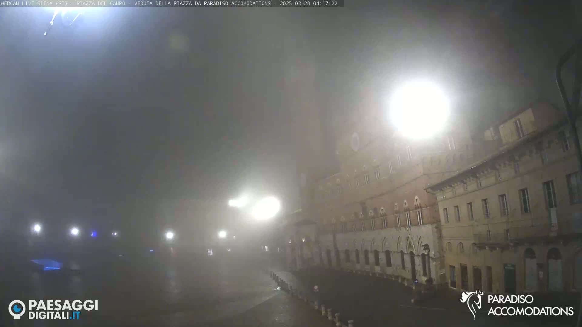 A foggy, nighttime view of a city square with buildings illuminated by streetlights.