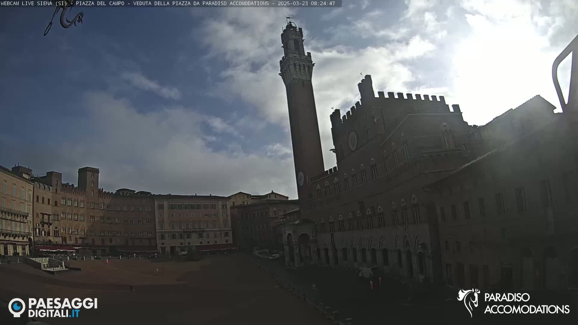 A mostly sunny day reveals a large, brick piazza in Siena, Italy, dominated by a tall tower and a grand palazzo.