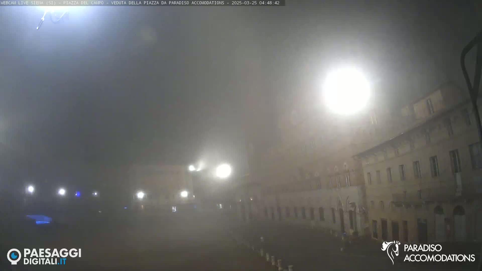 A foggy night scene shows a dimly lit plaza with buildings and streetlights.