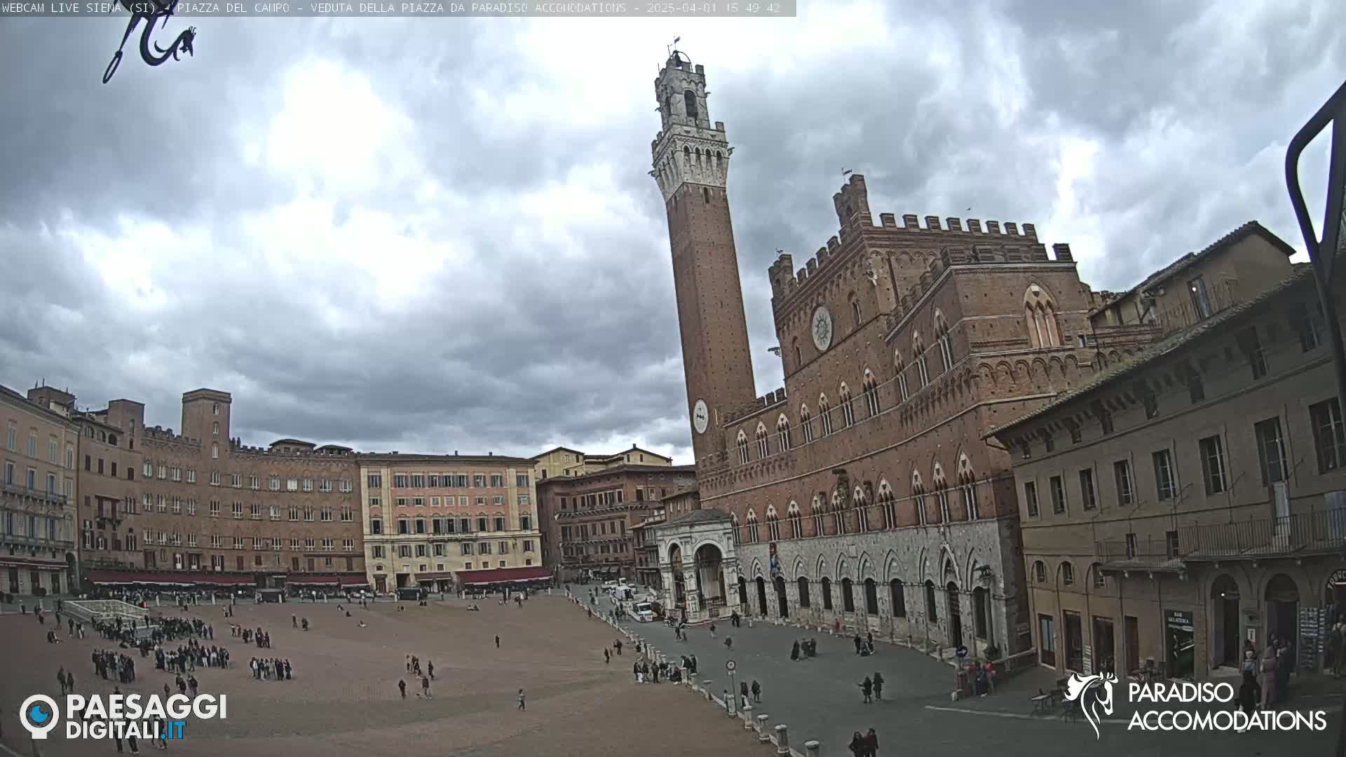 A large, brick public square is surrounded by historic buildings under a cloudy sky, with a tall tower prominently featured.