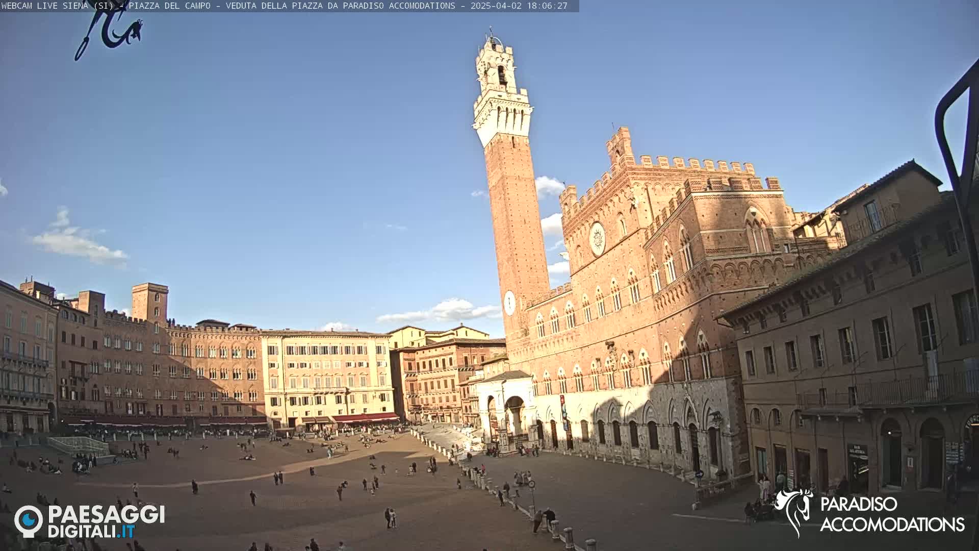 A large, mostly empty piazza in Siena, Italy, is surrounded by historic brick buildings under a mostly clear, sunny sky.